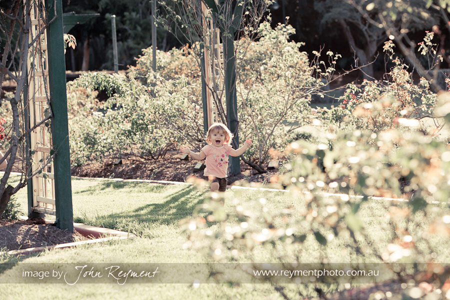 I'm sprung, Claire sees me hiding behind the roses in New Farm Park, by Brisbane family portrait photographer John Reyment