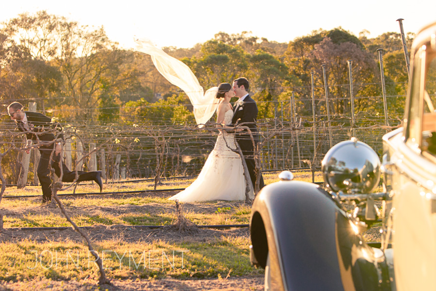 bride and groom, vines, wedding car at Sirromet Winery by Brisbane wedding photographer John Reyment